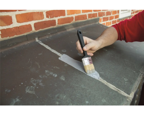 O persoană aplică un strat pe un acoperiș cu o pensulă.