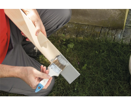 Bărbat care vopsește o scândură de lemn cu pensula și vopsea