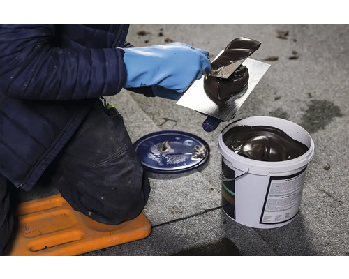 Acoperitorul aplică cu o mistrie masă de etanșare a acoperișului dintr-o găleată