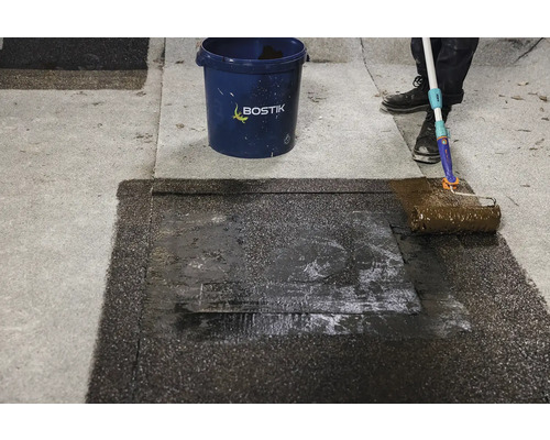 Aplicarea unui strat de acoperiș cu trafalet lângă găleata Bostik.