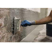 O persoană aplică șlam de etanșare pe un perete cu o perie.