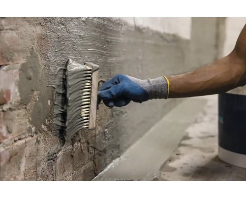O persoană aplică șlam de etanșare pe un perete cu o perie.