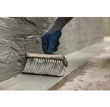 O persoană aplică cu o pensulă mortar impermeabil pe un perete.