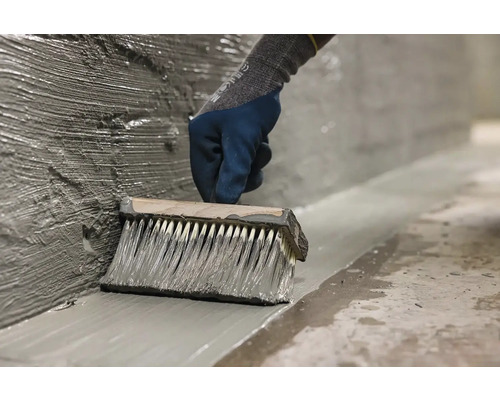 O persoană aplică cu o pensulă mortar impermeabil pe un perete.