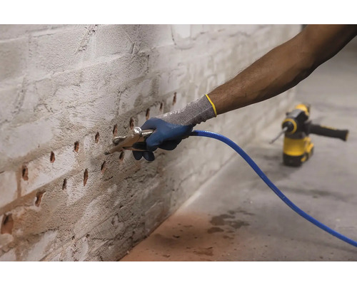 O persoană folosește o lance de injecție pe un perete de cărămidă cu găuri de foraj pentru a aplica tencuială de renovare.