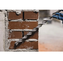 O persoană cu mănuși fixează o ancoră spiralată într-un zid de cărămidă.