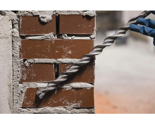 O persoană cu mănuși fixează o ancoră spiralată într-un zid de cărămidă.