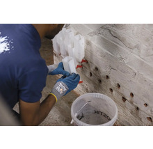 O persoană umple injectoarele cu rășină de injecție pentru reabilitarea zidăriei.