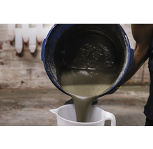 O persoană toarnă mortar dintr-o găleată într-un pahar gradat.