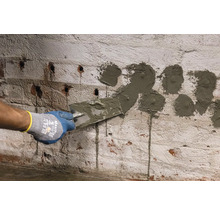 O persoană umple cu un cuțit de chit găuri într-un zid de cărămidă.