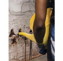 O persoană toarnă lichid dintr-o stropitoare într-un perete de cărămidă deteriorat.