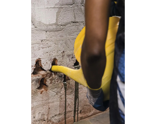 O persoană toarnă lichid dintr-o stropitoare într-un perete de cărămidă deteriorat.