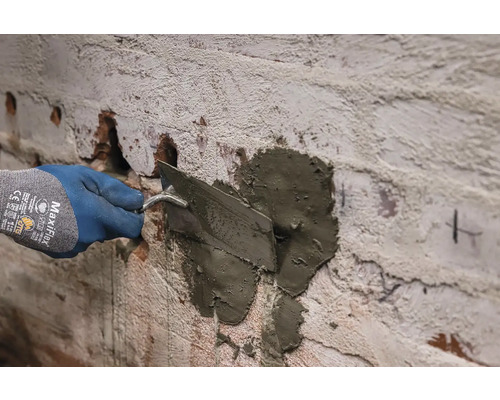 O mână cu mănușă aplică mortar pe un perete cu mistria.