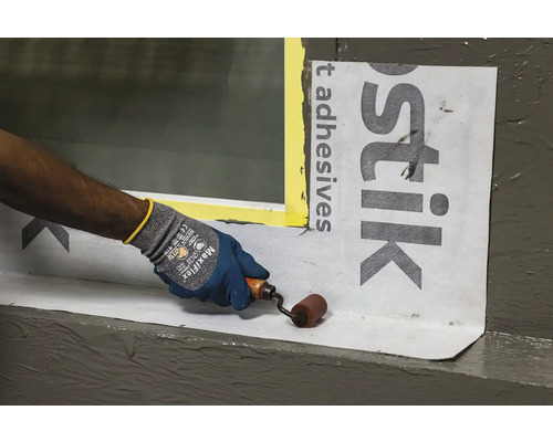 Artizan fixează banda de etanșare cu o rolă de presare pe o pervazul ferestrei.