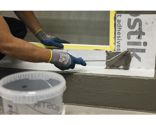 O persoană aplică etanșant cu o rolă pe o suprafață, cu o găleată de etanșant în prim-plan.