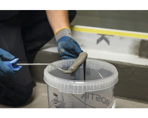 O persoană introduce o rolă de vopsea într-o găleată cu strat de acoperire.