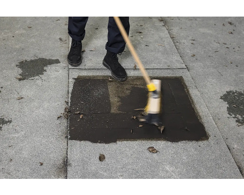 O persoană mătură un lichid închis la culoare pe o suprafață pavată cu o mătură.