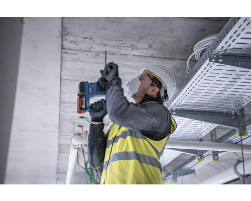 Artizan care găurește un tavan cu un ciocan rotopercutor.