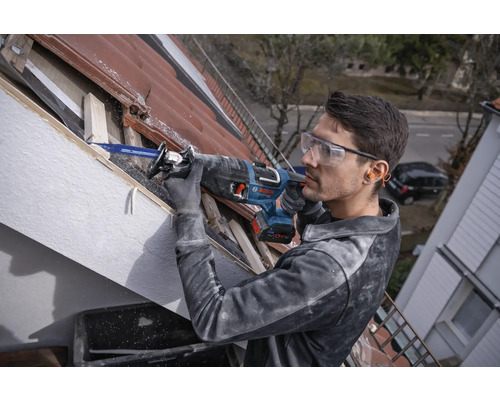 Un bărbat lucrează cu un ferăstrău sabie pe un acoperiș