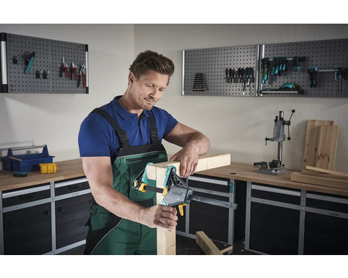 Un bărbat fixează lemn cu o menghină cu șurub într-un atelier.