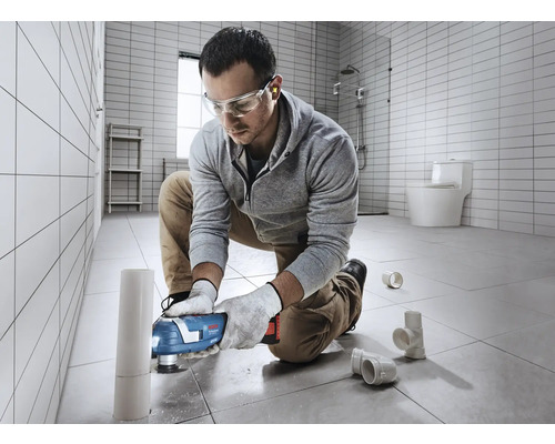 Un bărbat folosește un instrument multifuncțional în baie pentru a tăia o țeavă.