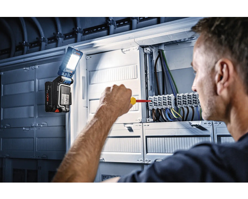 Un electrician lucrează la o cutie de distribuție cu o lampă de lucru Bosch.