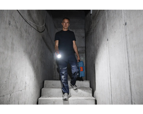 Bărbat coborând scări de beton cu o lanternă și o cutie de scule