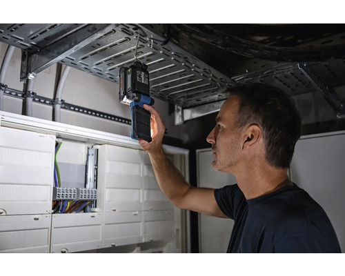 Un bărbat inspectează o instalație electrică cu o lampă de inspecție.