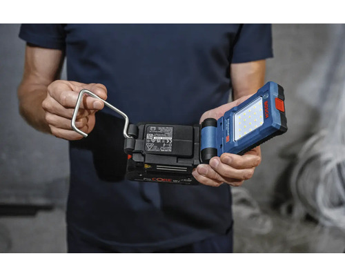 Un bărbat ține în mână o lampă de lucru cu acumulator cu cârlig de la marca Bosch.