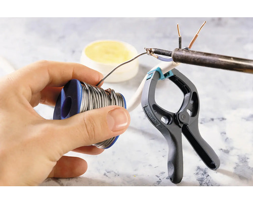 Bobină de cositor de lipit în mână, lucrări de lipire pe un cablu fixat cu o clemă