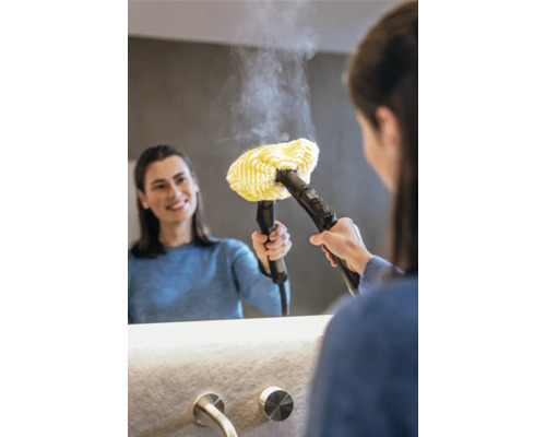 Femeie care folosește un aparat de curățat cu aburi cu un atașament de cârpă galbenă pe o oglindă din baie