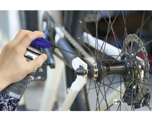 O persoană unge lanțul unei biciclete cu un spray de lanț.