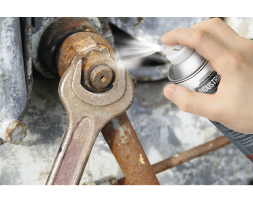 O persoană pulverizează un spray de îndepărtare a ruginii pe o piuliță ținută cu o cheie.