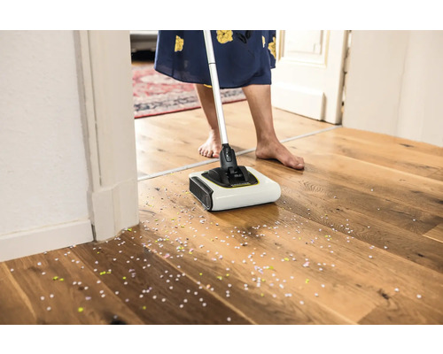 Mătură fără fir în uz pe o podea de lemn cu confetti