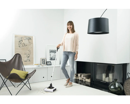 Femeie folosind un măturoi cu acumulator pentru curățare într-un living.