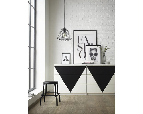 Fotografie de interior a unei camere cu o comodă cu modele geometrice, un scaun, postere și o lampă suspendată.