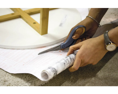 O persoană taie cu foarfeca o folie decorativă cu model de marmură pentru a înfrumuseța o masă.