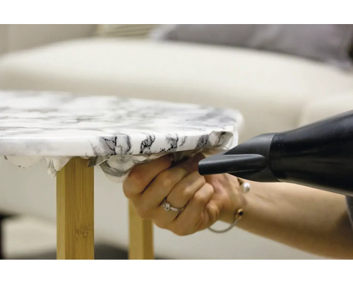 Aplicarea unei folii de mobilier cu un pistol cu aer cald pe o masă