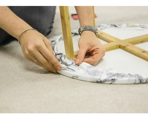 O persoană taie excesul de material de ambalare de pe o masă cu aspect de marmură și picioare din lemn.