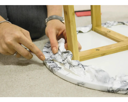 Tăierea foliei decorative pe o măsuță laterală cu aspect de marmură și picioare din lemn