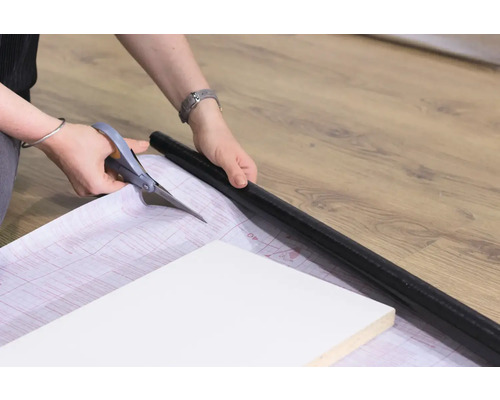 Persoană care taie cu foarfeca o folie pentru a lipi o piesă de mobilier