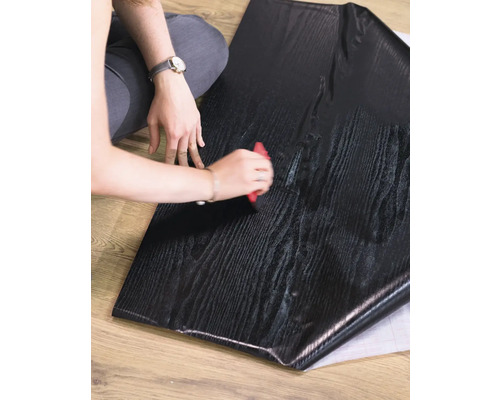 O persoană prelucrează o folie autoadezivă pentru mobilă cu aspect de lemn cu o racletă.