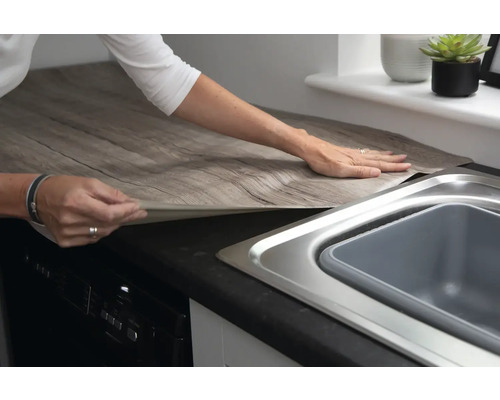 Femeia aplică folie decorativă cu aspect de lemn pe blatul de bucătărie