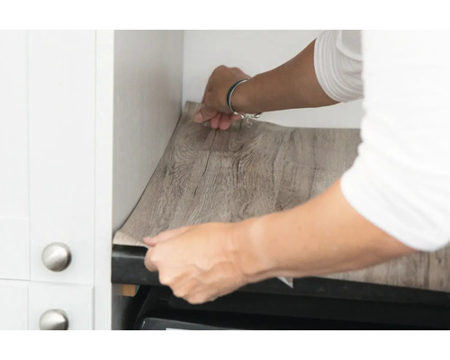 O persoană instalează folie autoadezivă cu aspect de lemn într-un dulap de bucătărie.