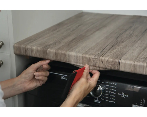 Persoană aplică folie autoadezivă cu aspect de lemn pe un blat de lucru