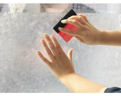 Persoană care aplică folie de intimitate cu racleta pe un panou de sticlă