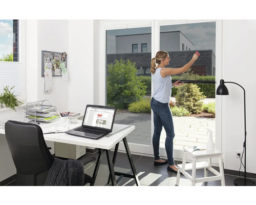 Femeie aplicând folie de protecție solară pe fereastră, birou în fundal