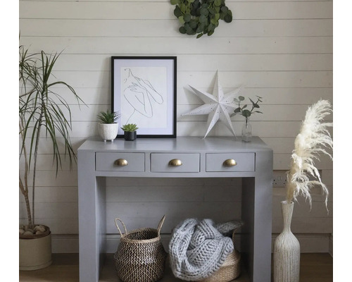 Interior decorativ cu consolă, artă, plante și coșuri într-o cameră luminoasă.