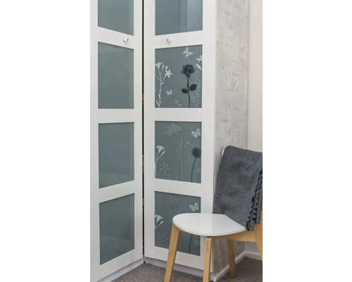 Dulap alb cu motive florale și uși de sticlă lângă un scaun cu o pătură gri