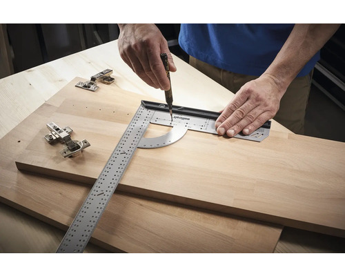 O persoană folosește un raportor de unghi și un stilou pentru a face marcaje pe o scândură de lemn lângă balamale.